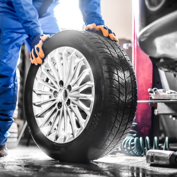 Auto mechanic working in garage and changing tire alloy rims. Car service repairs or maintenance.